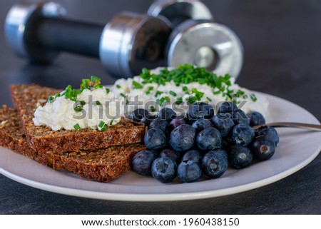 Fitness breakfast with low fat cottage cheese and bread served with fresh and ripe blueberries on a plate with dumbbells in the background
