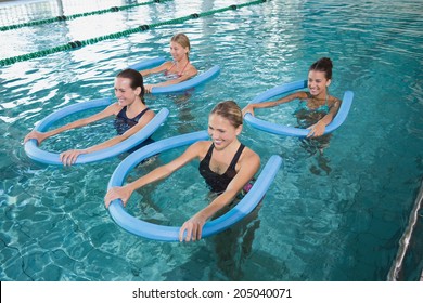Fitness class doing aqua aerobics with foam rollers in swimming pool at the leisure centre