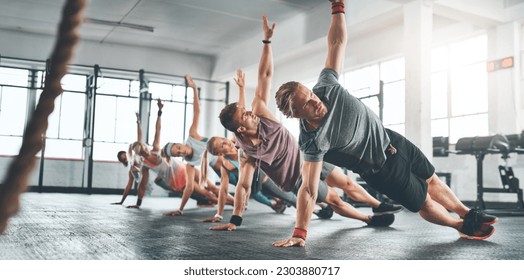 Fitness class, group and people doing a workout in the gym for health, wellness and flexibility. Sports, training and athletes doing a side plank exercise challenge together in sport studio or center - Powered by Shutterstock