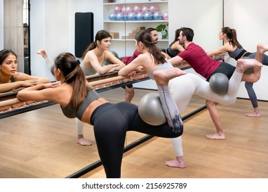 Fitness Class In A Gym Performing Hip Extension Exercises With A Pilates Ball Using The Barre Reflected In A Wall Mirror