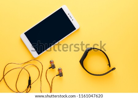 fitness concept with mobile phone, earphones and fitness tracker on yellow background top view