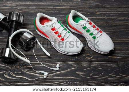 Fitness concept shoes for training, headphones, two metal dumbbells on a dark wooden background.