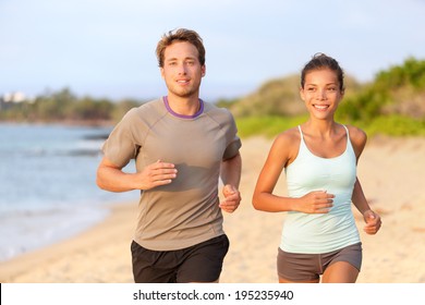 Fitness Couple Jogging Outside On Beach Smiling In Summer Sunset. Young Mixed Race Asian Female Model Running On Beach With Handsome Caucasian Male.