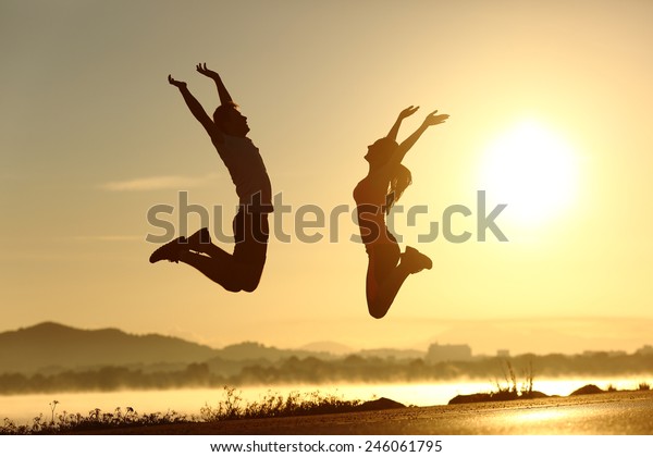 Fitness couple jumping happy at sunset with\
the sun in the\
background