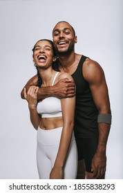 Fitness couple standing together against white background. Muscular man holding smiling female friend from behind.