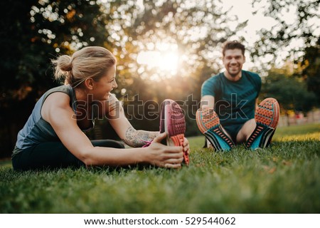 Fitness couple stretching outdoors in park. Young man and woman exercising together in morning.
