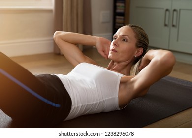 Fitness Determined Mature Woman Lying Doing Crunches At Home. Healthy Mid Woman Doing Exercises On Gym Mat. Concentrate Middle Age Lady Doing Daily Exercises Lying On The Floor In The Living Room.