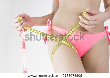 Fitness. diet. leg circumference. Woman in a pink swimsuit on a white background assures leg girth. Body measurement before medical diet. Leg circumference after fitness training