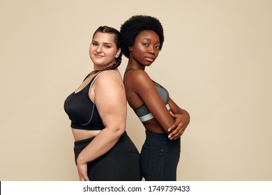 Fitness. Diverse Women In Sportswear Portrait. Caucasian And African Models In Sport Clothes Posing On Beige Background. Body Positive As Lifestyle. 