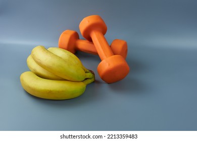 Fitness Dumbbells And A Bunch Of Bananas On A Gray Background. The Concept Is Fast Carbs Before And After The Workout.