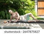 fitness elastic band, fit woman making yoga stretching exercises in open air in tropical yard, early morning. Resort vacation getaway. Summer holidays time. 