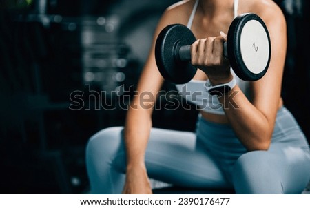 A fitness enthusiast training at the gym, lifting weights and performing exercises with dumbbells to build up her strength and maintain her health and beauty, fitness GYM dark background