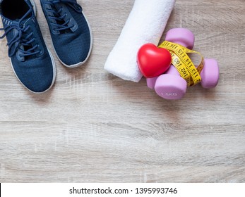 Fitness Equipment With Dumbbells, Shoes, Measuring Tape, Heart And Towel On Wooden Floor Background. Top View From Above. Health And Exercise Concept With Copy Space