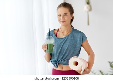 fitness equipment, sport and healthy lifestyle concept - smiling young woman with cup of smoothie and exercise mat at yoga studio or gym
