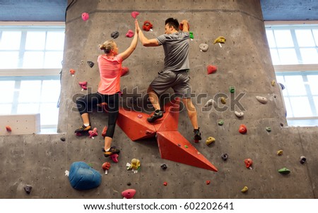 fitness, extreme sport, bouldering, people and healthy lifestyle concept - man and woman exercising at indoor climbing gym and making high five gesture