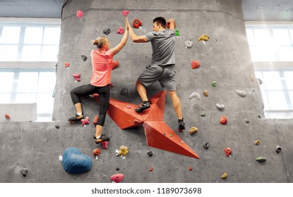 fitness, extreme sport and healthy lifestyle concept - young man and woman bouldering on a rock climbing wall at indoor gym and making high five gesture - Powered by Shutterstock