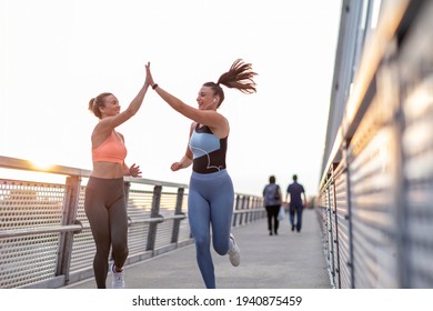 Fitness female friends in sportswear high five to each other while run together