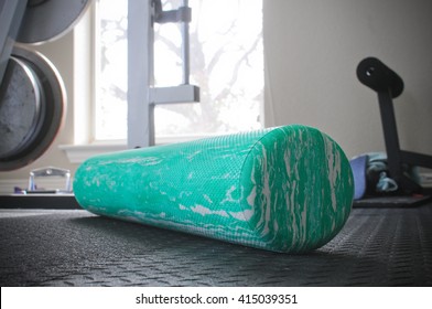 Fitness foam roller sitting on indoor gym floor with weights in background.