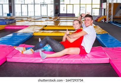 Fitness, fun, leisure and sport activity concept - Happy cheerful couple sits together on a trampoline indoors