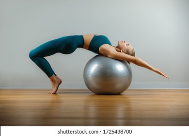 Fitness girl with fitball on in the gym room on gray background. Kinky body, flexibility and stretching. Copy space