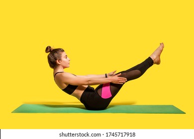 Fitness Girl With Hair Bun In Tight Sportswear Doing Sport, Physical Training On Gym Mat, Reaching Hands To Feet, Exercising Abdominal Muscles, Warming Up. Studio Shot Isolated On Yellow Background