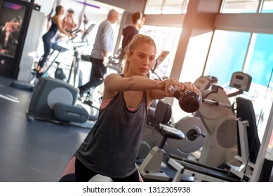 Fitness Girl Lifting Dumbells During An Exercise Class In A Gym While Group Of People Running On Treadmills In The Background 