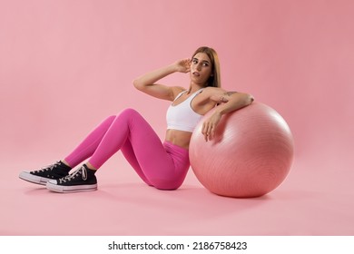 Fitness Girl In Pink Clothes Lying On The Floor Next To A Yoga Ball, Isolated On A Pink Background.