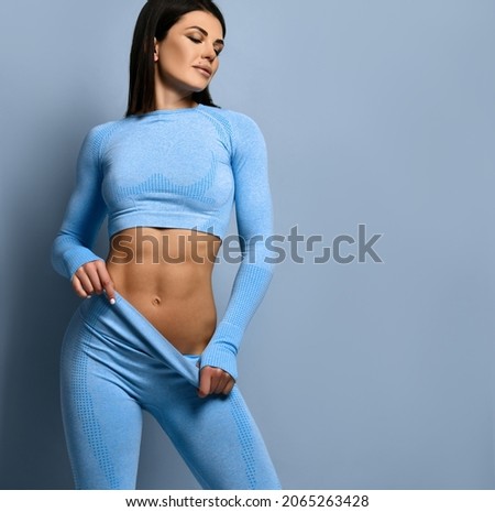 Fitness girl portrait. Woman in fashion sportswear, standing on a blue background, after a workout. Girls with a strong muscular body come up, show their pumped up abs.