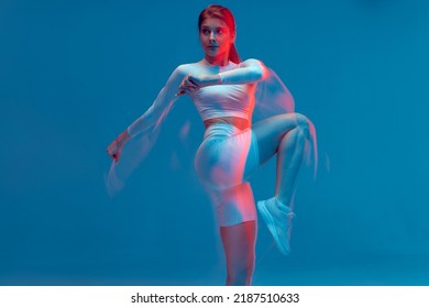 Fitness girl rasing hips, doing warm up exercise for legs on blue backdrop. Long exposure, motion blur. Sports workout