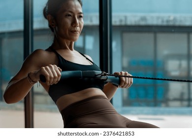 Fitness girl workout on indoor rower at the gym, doing exercises on rowing machine near the window, woman exercising in fitness club, selective focus