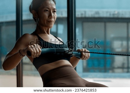 Fitness girl workout on indoor rower at the gym, doing exercises on rowing machine near the window, woman exercising in fitness club, selective focus