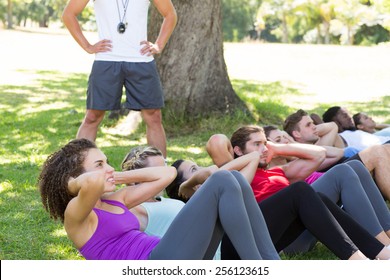 Fitness group doing sit ups in park with coach on a sunny day - Powered by Shutterstock