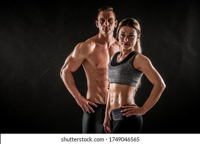 Fitness in gym, sport and healthy lifestyle concept. Couple of athletic man and woman showing their trained bodies on dark background. Two bodybuilder models standing and demonstrating tight muscles. - Powered by Shutterstock