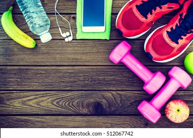Fitness, healthy and active lifestyles Concept, dumbbells, sport shoes, bottle of waters, smartphone with headphone, banana and apples on wood background. copy space for text. Top view - Shutterstock ID 512067742