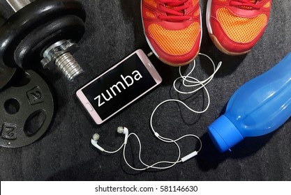 Fitness, Healthy And Active Lifestyles Concept. Dumbbells, Sport Shoes, Smart Phone With Earphone And Water Bottle Gym Floor With Word Zumba