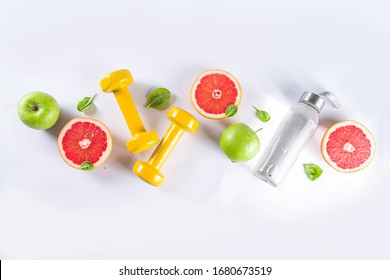 Fitness And Healthy Food Lifestyle Concept. Dumbbells, Diet Fruit And Vegetable Lunch Box, Water And Jump Rope On White Background. Flatlay Image, Top View Copy Space