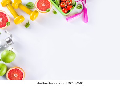 Fitness And Healthy Food Lifestyle Concept. Dumbbells, Diet Fruit And Vegetable Lunch Box, Water And Jump Rope On White Background. Flatlay Image, Top View Copy Space