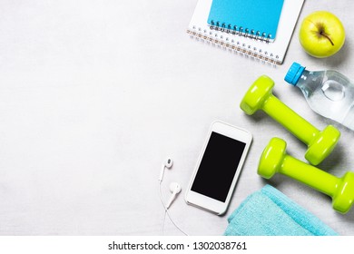 Fitness And Healthy Lifestyle Concept. Dumbbells, Measuring Tape, Water And Smartphoneon Light Background. Flatlay Image.