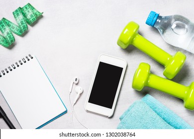 Fitness And Healthy Lifestyle Concept. Dumbbells, Measuring Tape, Water And Smartphoneon Light Background. Flatlay Image.