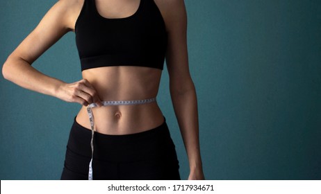 Fitness home banner. Home training in self-isolation. A slender girl in sportswear measures her body and waist with a meter. Losing weight. Copy space. Concept of sports, lifestyle, health