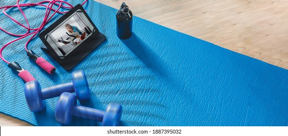 Fitness at home, remote training with virtual instructor. Woman in sportswear sitting on the floor with dumbbells laptop at home. Sports and recreation concept in lockdown with fitness apps online - Powered by Shutterstock