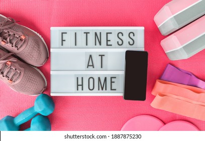 Fitness At Home Sign With Mobile Phone On Pink Yoga Mat, Running Shoes, Kettlebell Weight And Dumbells Resistance Bands And Sliders For Pilates Online Class. Exercise Indoors For Women.