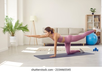 Fitness At Home.Young Sporty Woman Exercising At Home Standing On All Fours And Lifting Leg And Arm. Girl In Comfortable Sportswear Does Morning Exercises And Yoga On Sports Mat In Living Room.