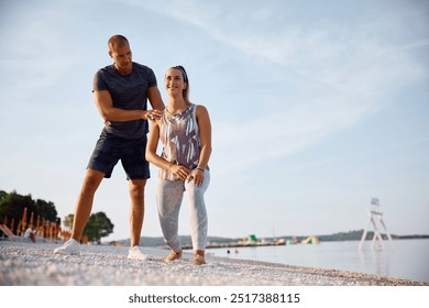 Fitness instructor assisting a woman during sports training on the beach. Copy space. - Powered by Shutterstock