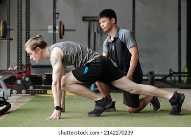 Fitness Instructor Correcting Young Man Doing Mountain Climber Exercise With Core Sliders