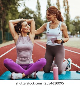 A fitness instructor encourages a woman during an outdoor stretching session on a track. The positive interaction emphasizes healthy lifestyle and motivation. - Powered by Shutterstock