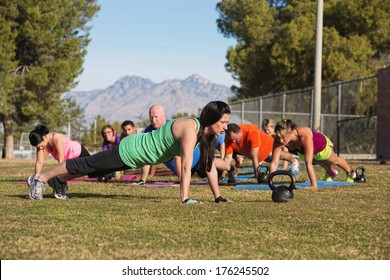 Fitness instructor leading group in push up exercises outdoors - Powered by Shutterstock