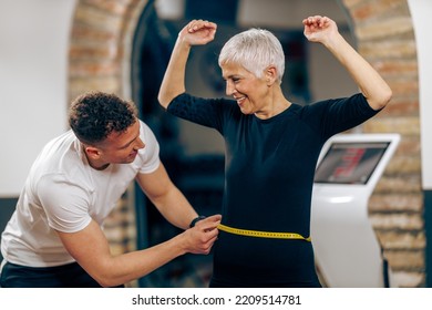 Fitness instructor measuring senior woman's waist before working out in the gym.