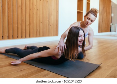 Fitness lady beginning yoga practice with private teacher at home class, working out with professional female yogi instructor. Trainer helps student to do Salabhasana exercise, Locust pose