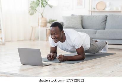 Fitness Lessons Online. Young Black Man Exercising At Home, Using Laptop, Copy Space